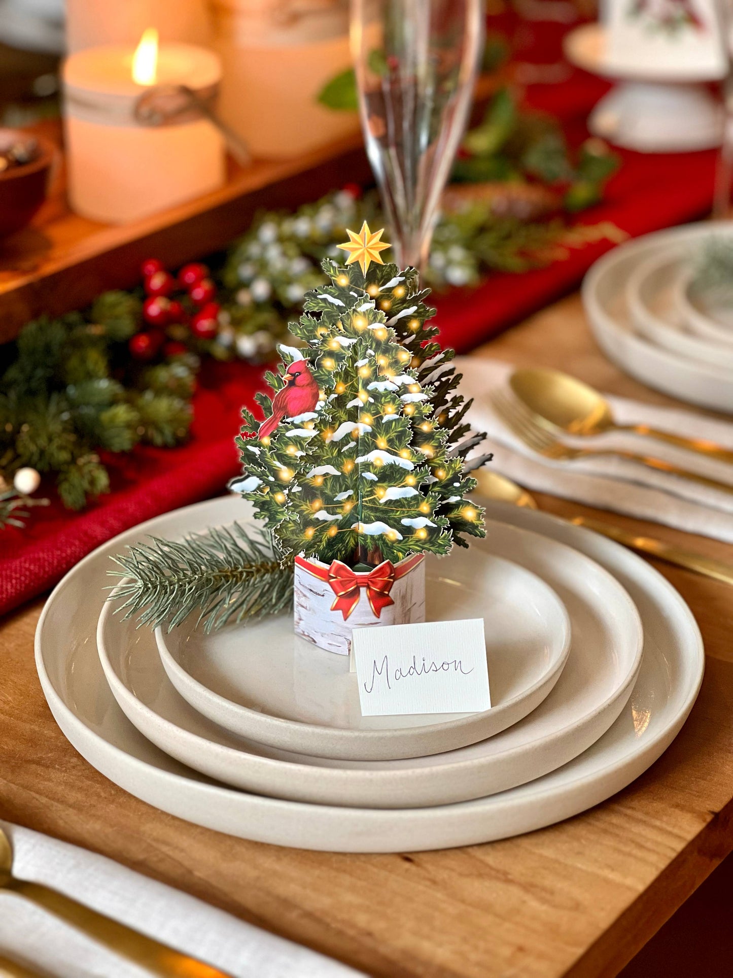 Merry Mini Tree Pop-up Greeting Card on holiday table; festive stationery store product with glowing snow-dusted tree and cardinal.