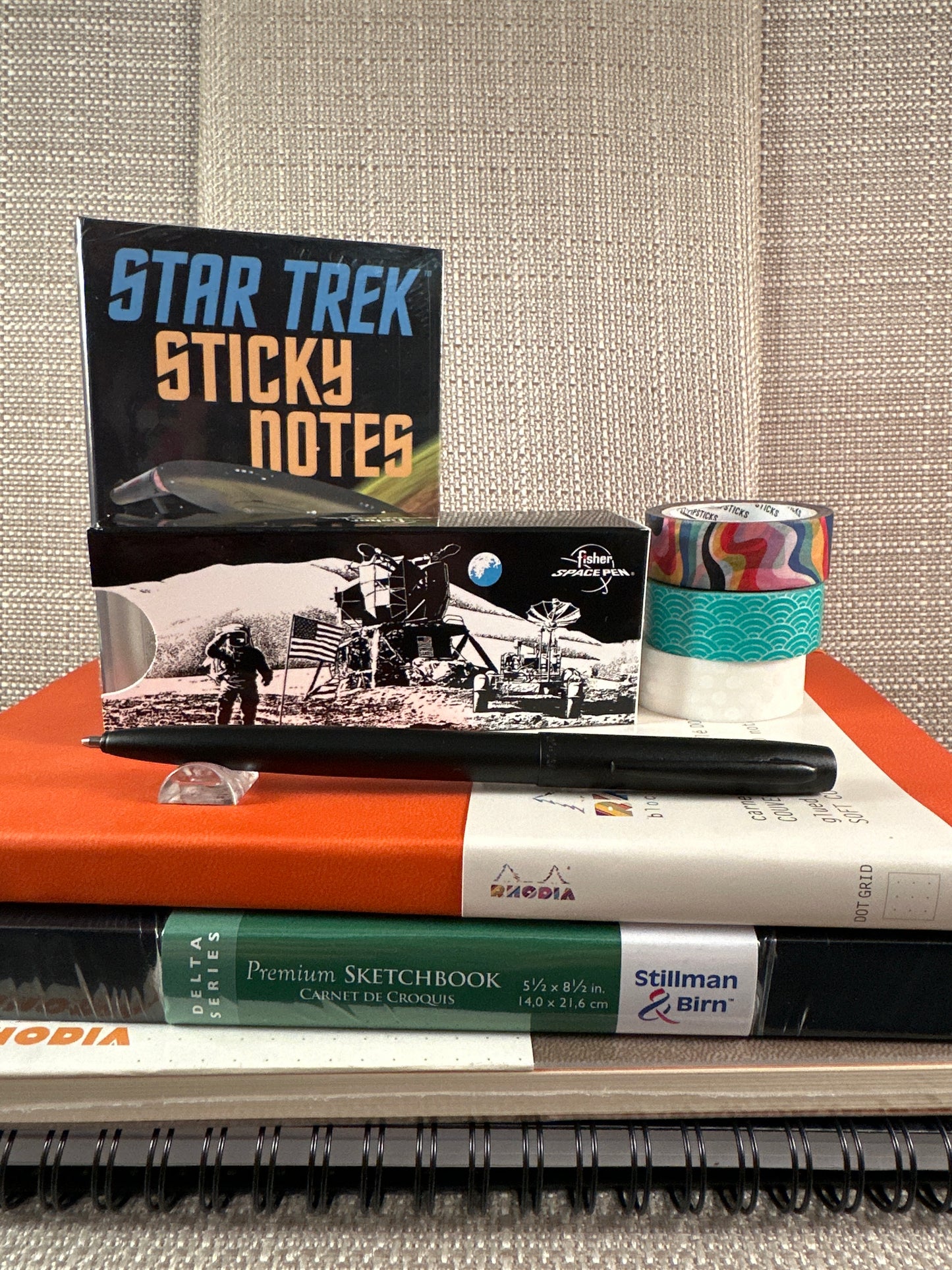 Fisher Space Pen Military edition on stacked sketchbooks with Star Trek sticky notes and washi tape, available at stationery store.