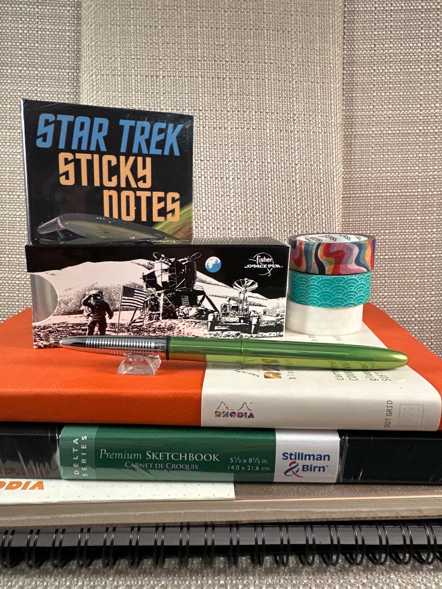 Collection of stationery items including Star Trek sticky notes, Fisher Space Bullet Pen, and sketchbook stack.