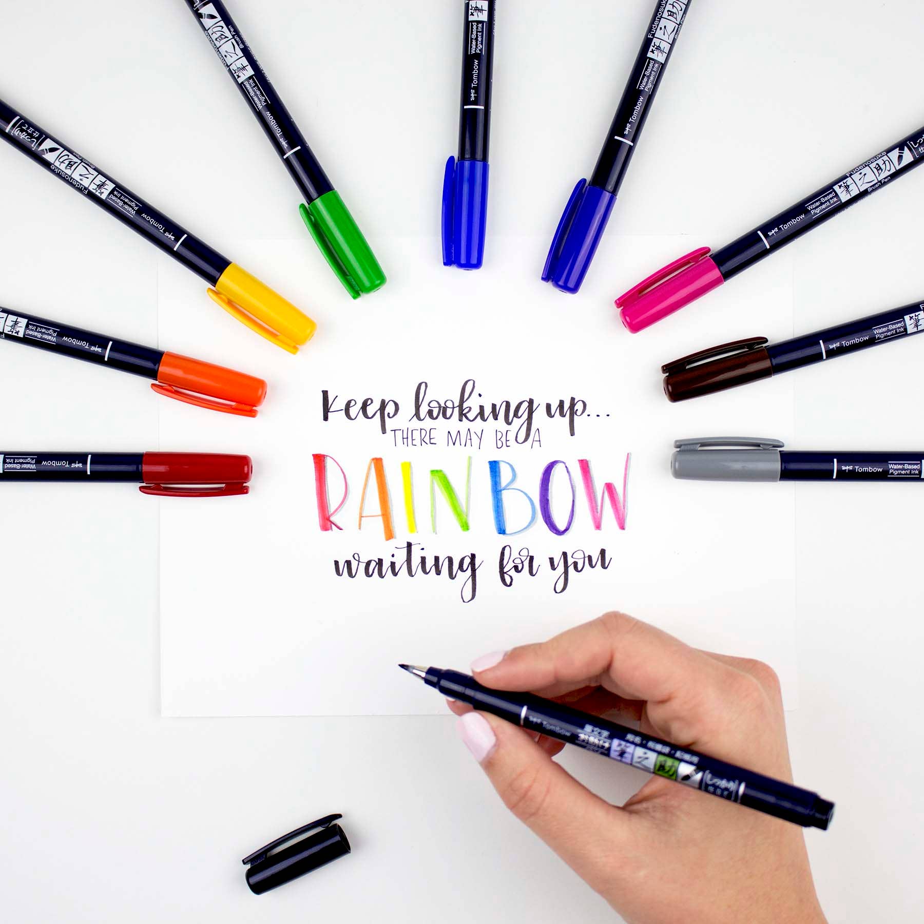 Person using Fudenosuke Calligraphy Brush Pen with colorful ink for rainbow lettering, available at stationery store.