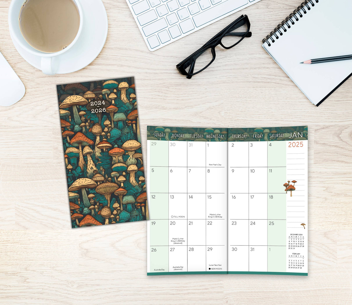 2025 Mighty Mushrooms Pocket Planner open on a desk with coffee and stationery, showcasing monthly calendar layout.