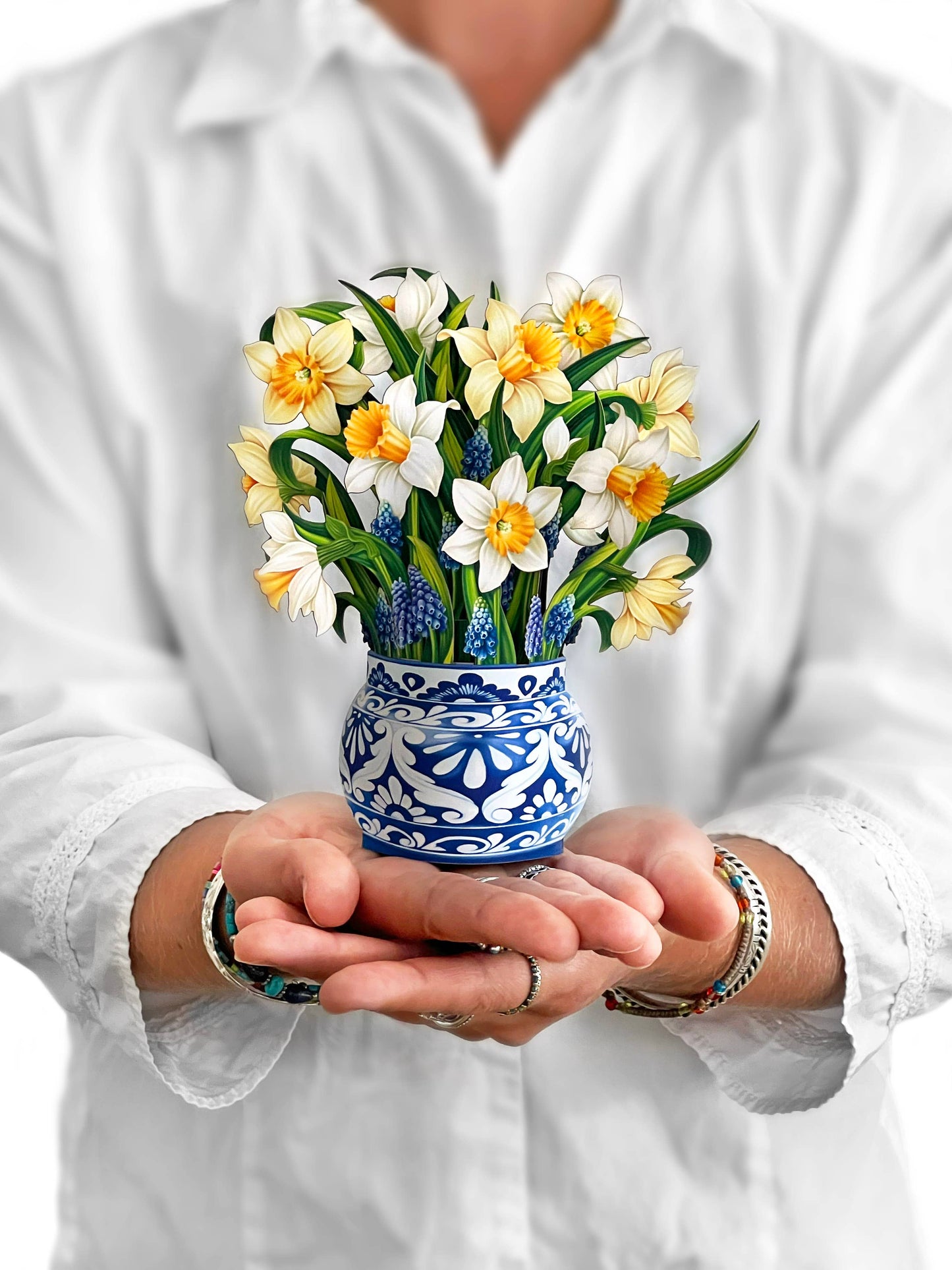 Alt Tag: Mini English Daffodil pop-up bouquet in blue vase, held by hands, from stationery store. Yellow and cream blossoms symbolize hope and healing.