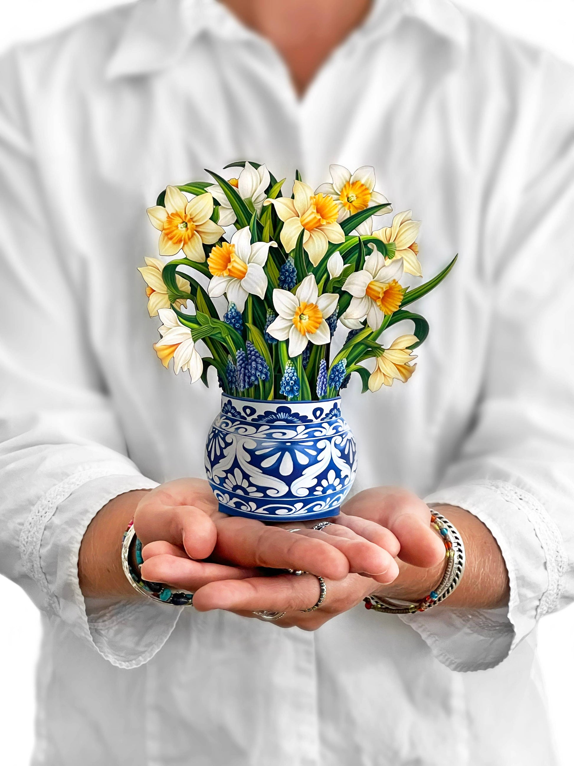 Alt Tag: Mini English Daffodil pop-up bouquet in blue vase, held by hands, from stationery store. Yellow and cream blossoms symbolize hope and healing.
