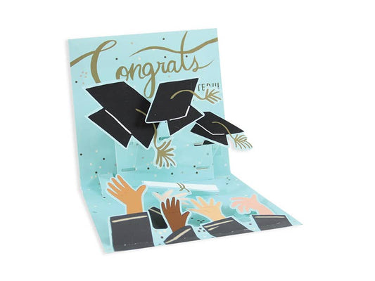 Pop-up graduation card featuring colorful artwork with hats and hands, celebrating graduation with a "Congrats" message.