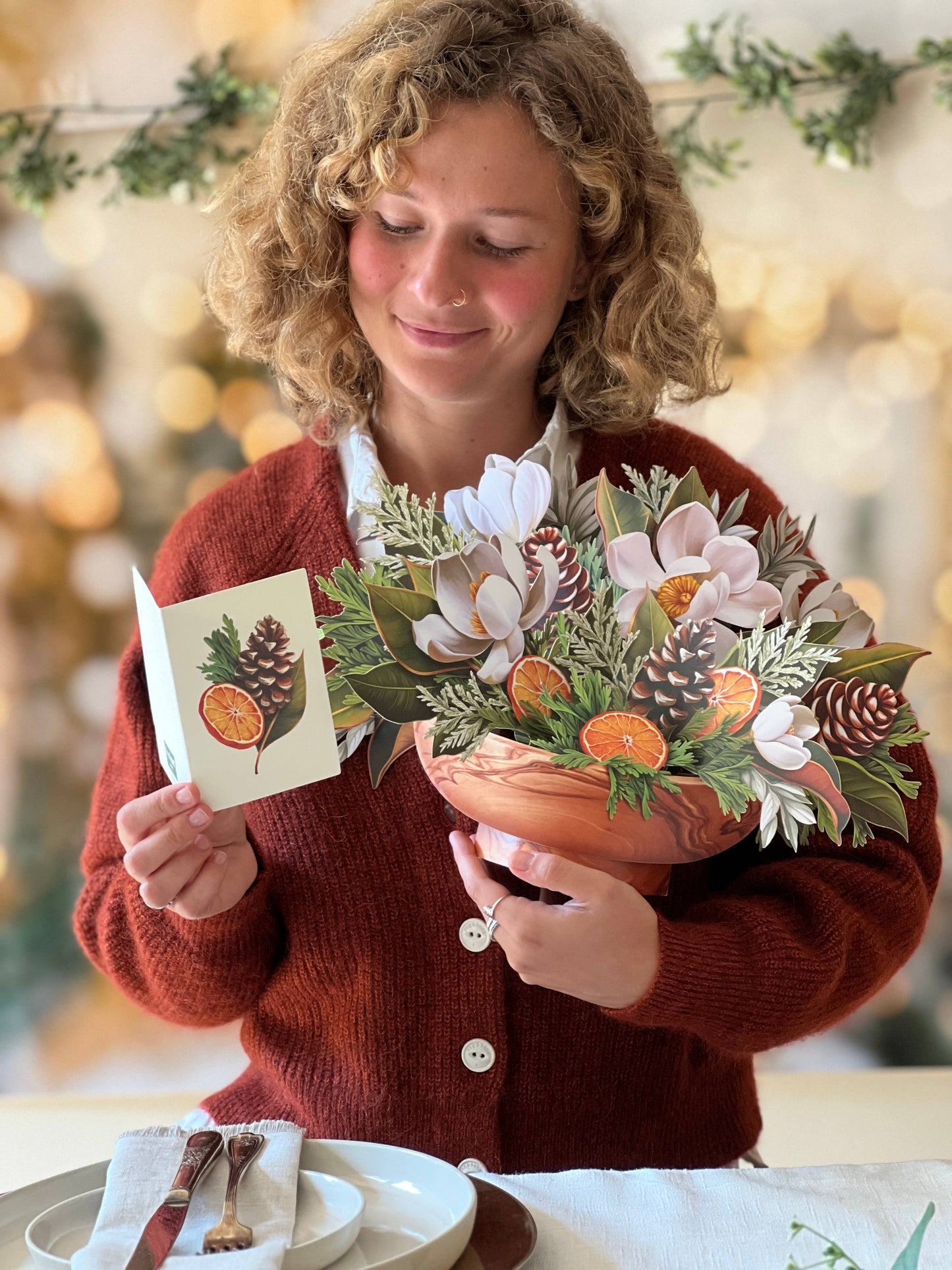 Woman holding Winter Magnolia Pop-up Greeting Card with magnolias, orange slices, and pine cones, from stationery store.