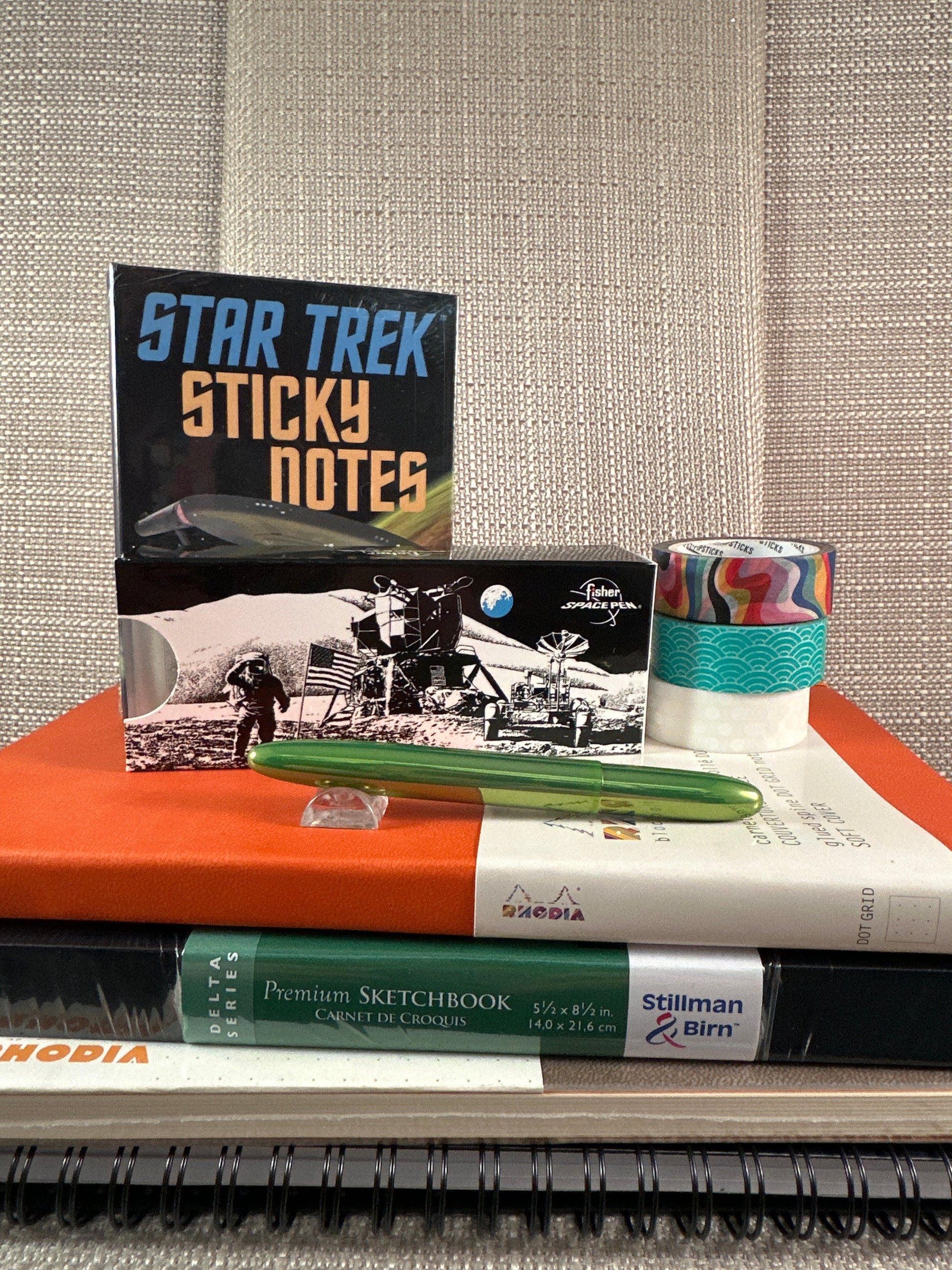 Stationery items including Star Trek sticky notes, a green Fisher Space Pen, colorful tape, and sketchbooks on a desk.