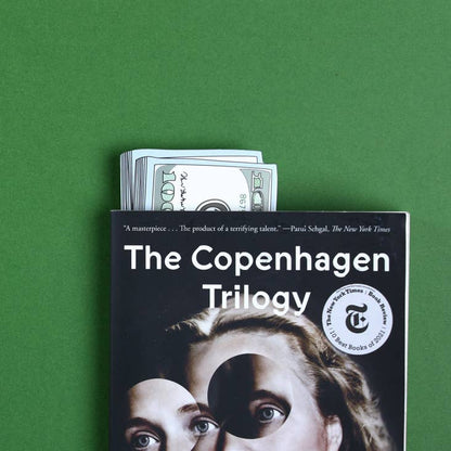 Stack of Cash die-cut bookmark sticking out from 'The Copenhagen Trilogy' book, available at our stationery store.