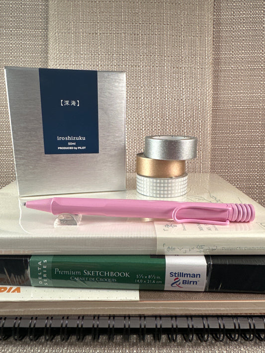 Pink LAMY Safari Ballpoint Pen displayed with sketchbooks and Washi tape in a stationery store setting.