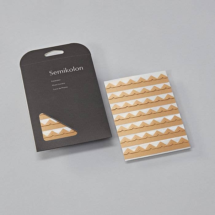 Self-adhesive photo corners in black packaging, ideal for scrapbooks and albums. Available at stationery stores. Size: 0.7 x 0.7 in.