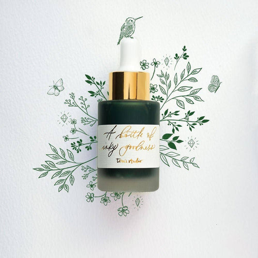 Emerald Calligraphy Ink in glass bottle with gold label and pipette, surrounded by leaves, available at stationery store.