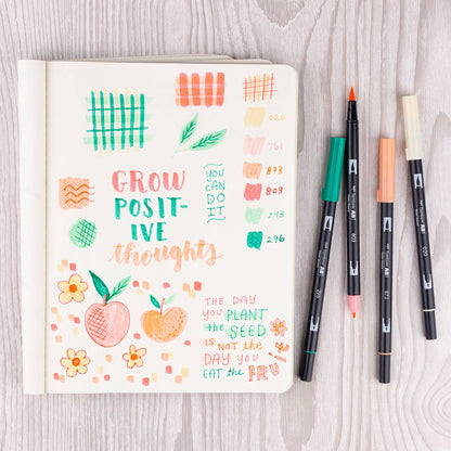 Notebook with colorful designs and quotes drawn using Dual Brush Pen Art Markers Just Peachy 6-Pack from a stationery store.