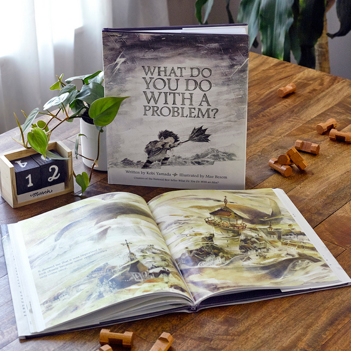 Book 'What Do You Do With A Problem?' displayed on a wooden table in a stationery store, offering a unique reading experience.