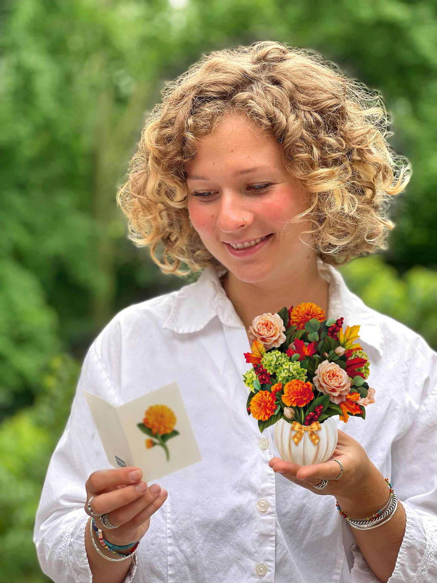 Woman holding Mini Pumpkin Spice Pop-up Greeting Card and flower card from stationery store, enjoying the vibrant design outdoors.