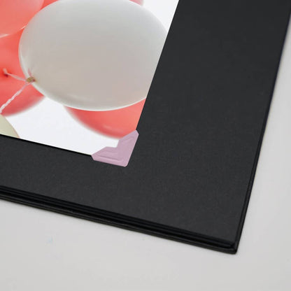 Photo corners mounting a picture in a black album. Self-adhesive, acid-free corners available at stationery store for photo albums or scrapbooks.