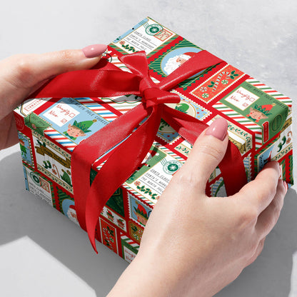 Gift wrapped in North Pole Bound paper with red ribbon, showcasing Christmas designs. Available at stationery stores for holiday wrapping.