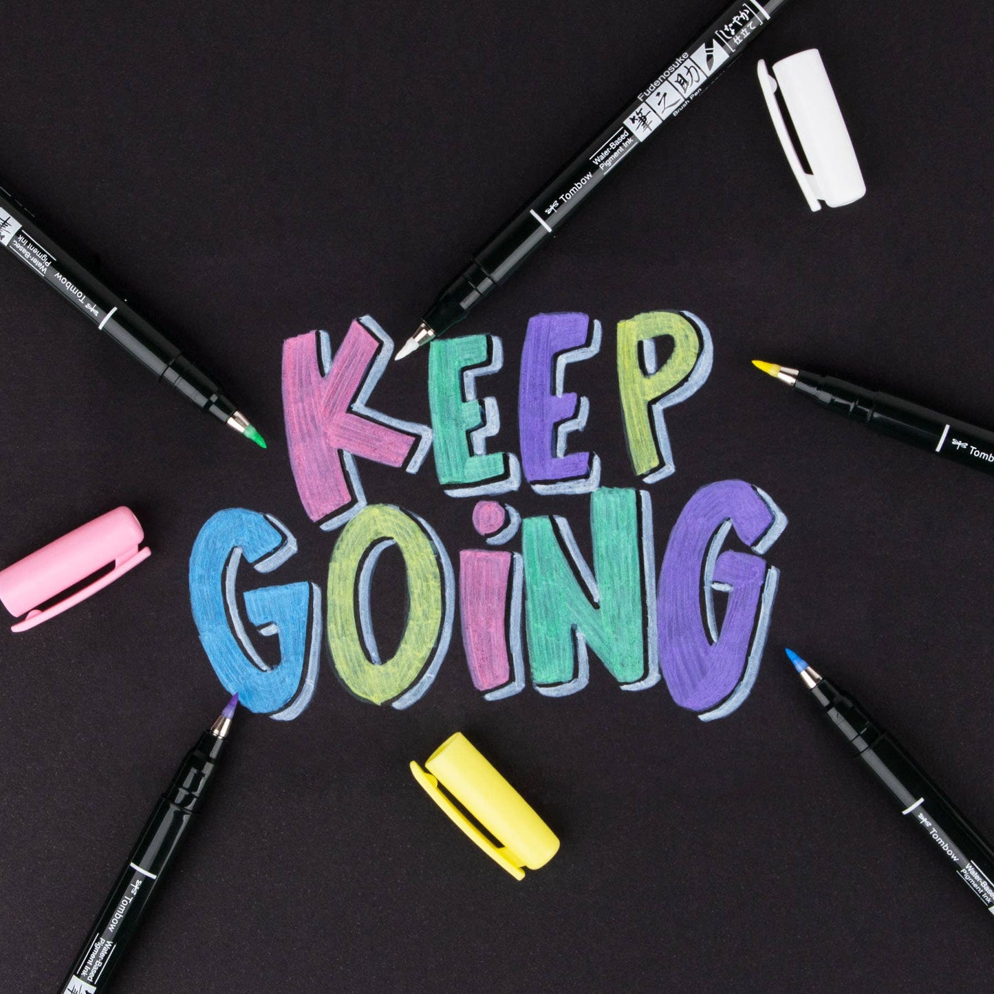 Fudenosuke Pastel Brush Pens writing 'Keep Going' on dark paper; ideal for stationery store displays.