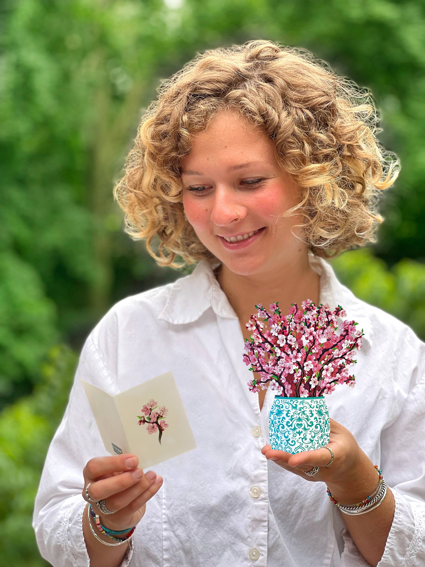 Woman holding Mini Cherry Blossom Pop-up Greeting Card with a floral design, available at stationery store.