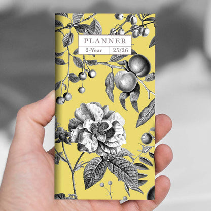 Close-up of hand holding 2025-2026 Yellow Botanical Small Monthly Pocket Planner with floral cover, perfect for a stationery store.