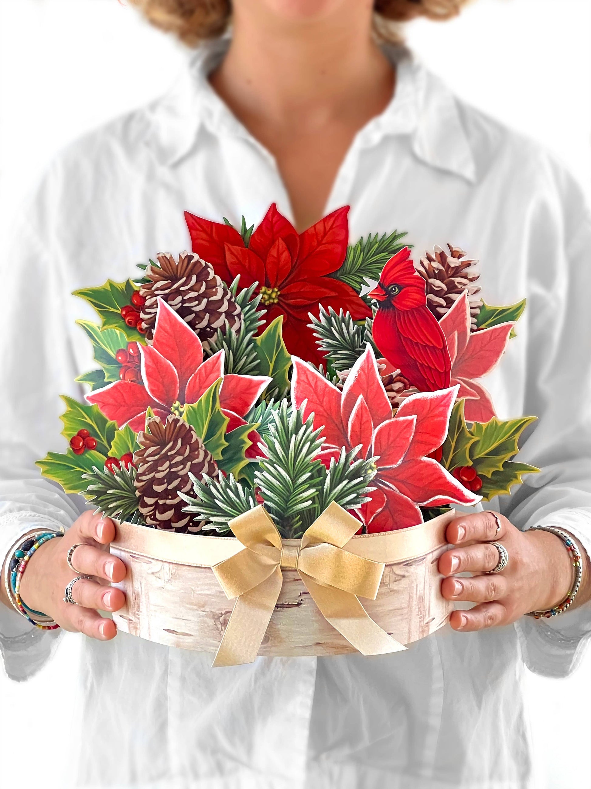 Alt Tag: Woman holding Birch Poinsettia Pop-up Greeting Card with pinecones, holly, and cardinal. Perfect for winter from stationery store.